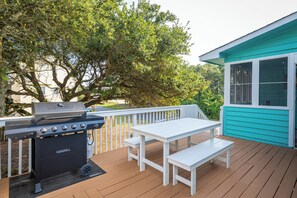 Terraza al aire libre con una parrilla, una mesa blanca y bancos.