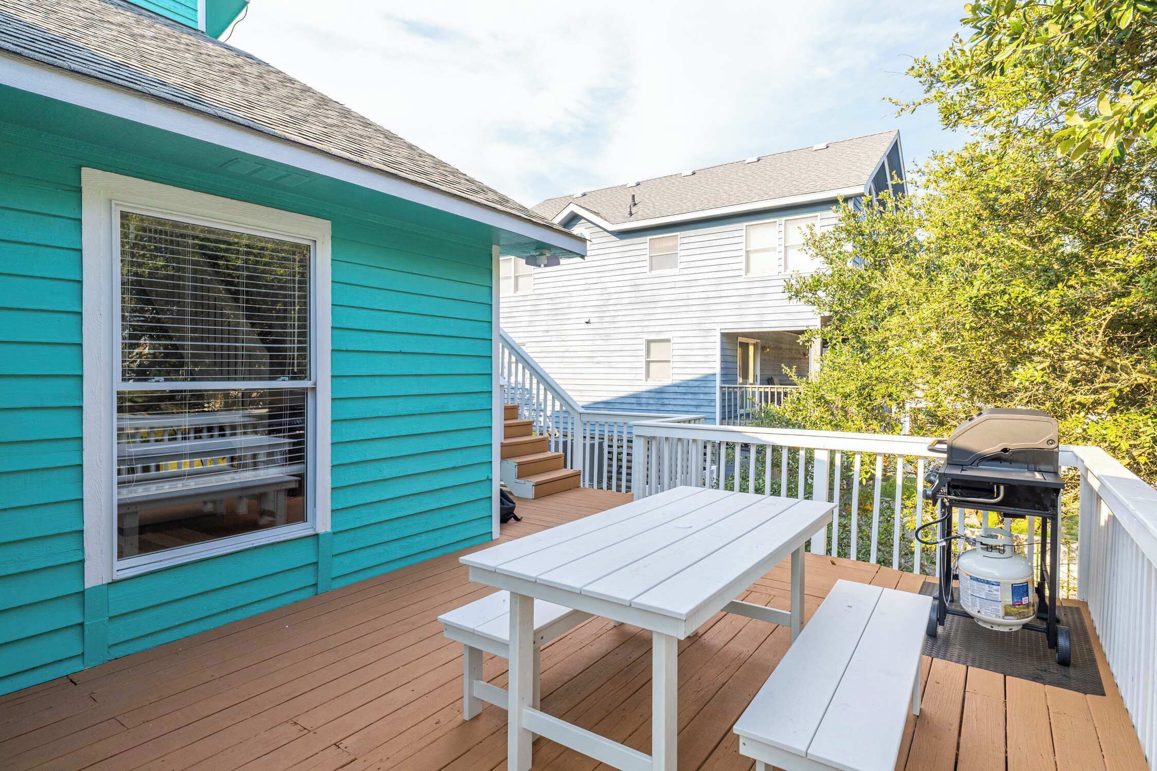 A deck with a white table and bench, a grill, and a window with blinds.