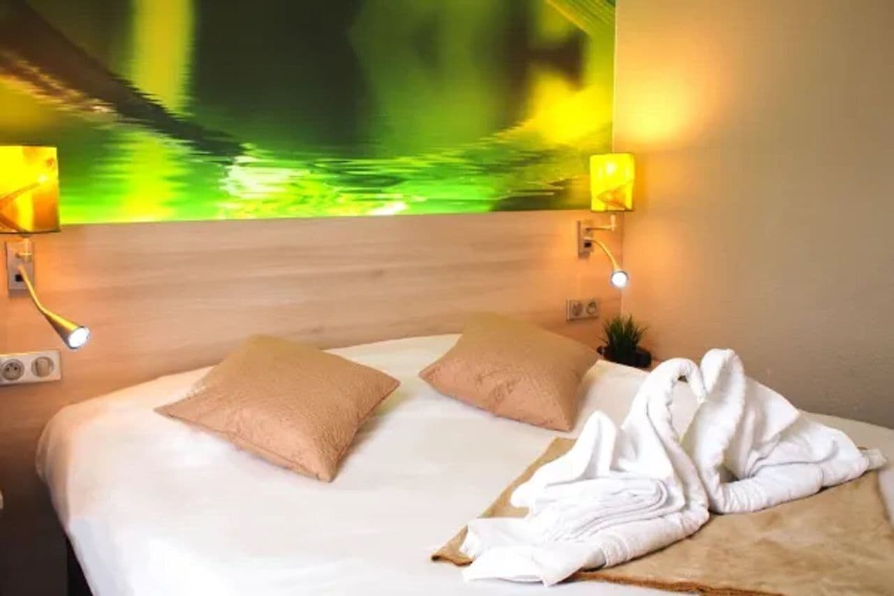 Ein Hotelzimmer mit einem Bett, zwei Kissen, einem Handtuch und Wandleuchten.