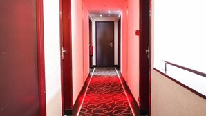 A hotel corridor with a red carpet and doors on both sides. - Hotel Inn Design Resto Novo Alencon (Valframbert)