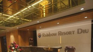 Un comptoir d’accueil au Rainbow Resort Diu, doté d’un design moderne, avec une grande enseigne au-dessus et une statue d’éléphant décorative.