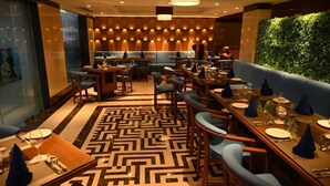 Un restaurant dont l’agencement intérieur ressemble à un labyrinthe, avec des tables en bois, des sièges rembourrés en tissu bleu et un mur vert agrémenté de luminaires verticaux.