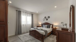 Een slaapkamer met een houten bed, nachtkastjes met lampen, een grote spiegel en uitzicht buiten door dunne gordijnen.