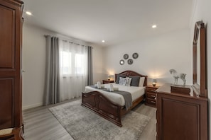 Ein Schlafzimmer mit einem Holzbett, Nachttischen mit Lampen, einem großen Spiegel und Blick ins Freie durch leichte Vorhänge.