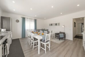 Eine moderne Küche mit integriertem Backofen, ein Essbereich mit Tisch für vier Personen und ein Wohnbereich mit Sofa und Couchtisch.