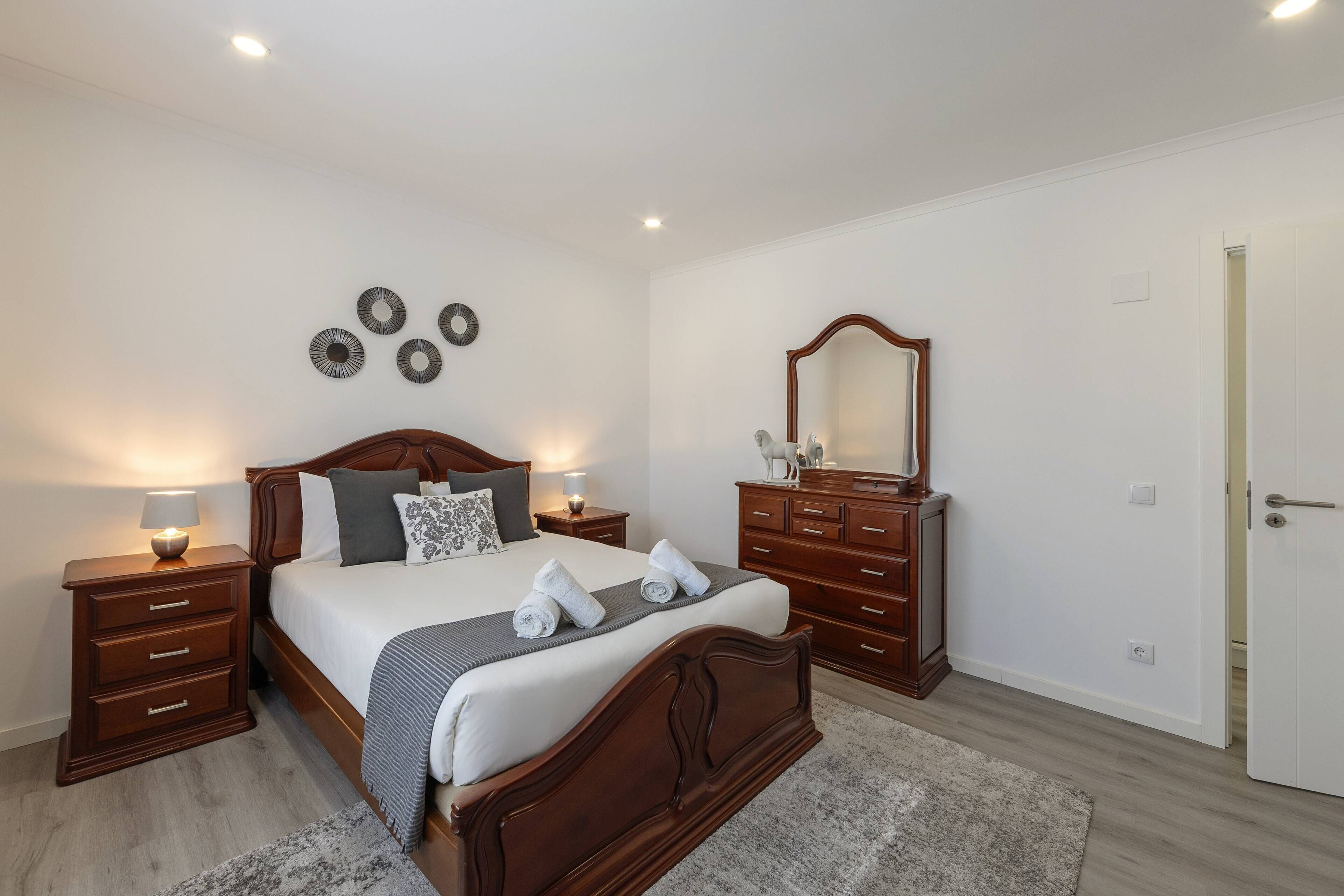 Une chambre d’hôtel avec un lit en bois, des tables de chevet avec des lampes, une commode, un miroir et une porte.