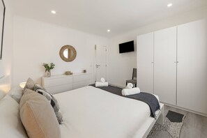 A modern bedroom with a large bed, a TV, a wardrobe, and a mirror. - Casa Amável - Vila Serena (Caldas da Rainha)
