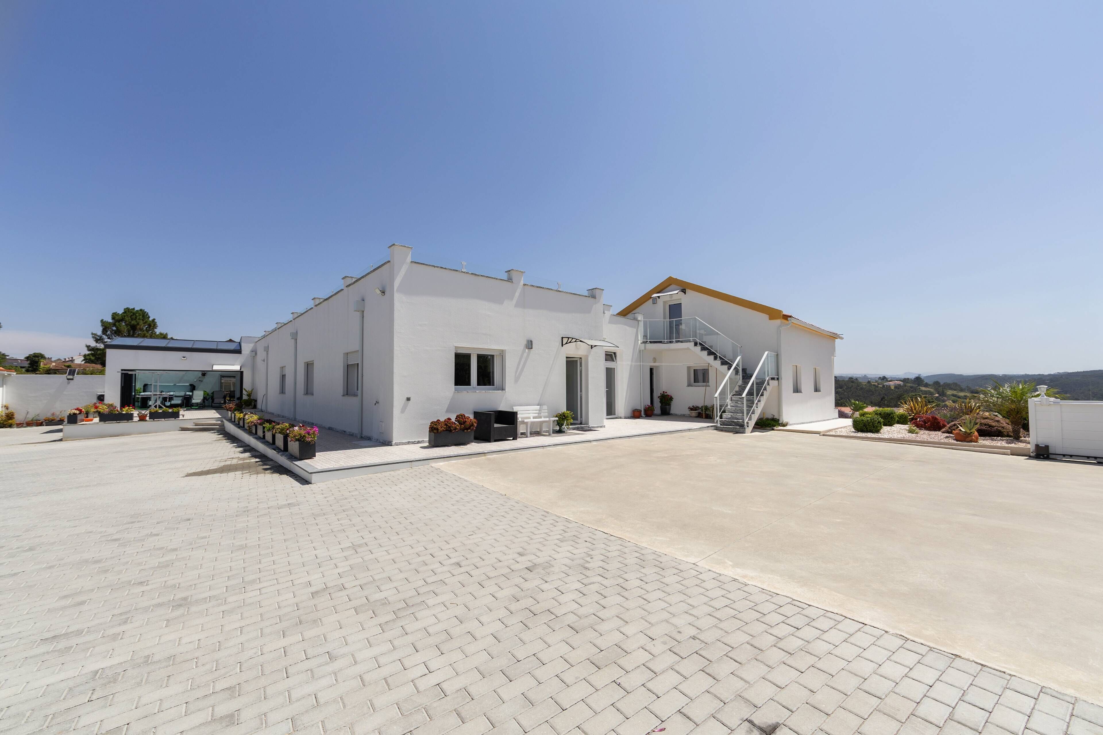 A modern two-story building with a flat roof, a staircase leading to the upper floor, and a paved driveway.