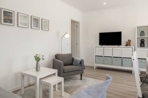 A modern living room with a grey sofa, a white table, a TV on a stand, and a cabinet with storage drawers. - Casa Amável - Vila Serena (Caldas da Rainha)