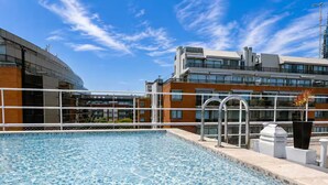 A swimming pool with clear blue water, surrounded by a white fence and a modern building with multiple windows and balconies. - Elegante departamento frente al Dique (Buenos Aires)