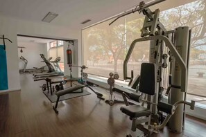 Ein Fitnessraum mit verschiedenen Trainingsgeräten, großen Fenstern und Holzboden.
