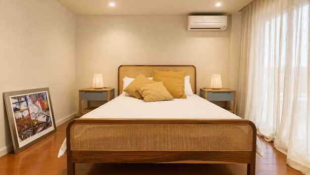 A bedroom with a wooden bed, two bedside tables, a framed picture, and an air conditioning unit. - Elegante departamento frente al Dique (Buenos Aires)