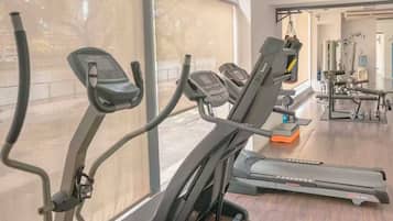 Une salle de sport équipée de nombreux appareils d’exercice, dotée de grandes fenêtres et offrant une vue sur l’extérieur.