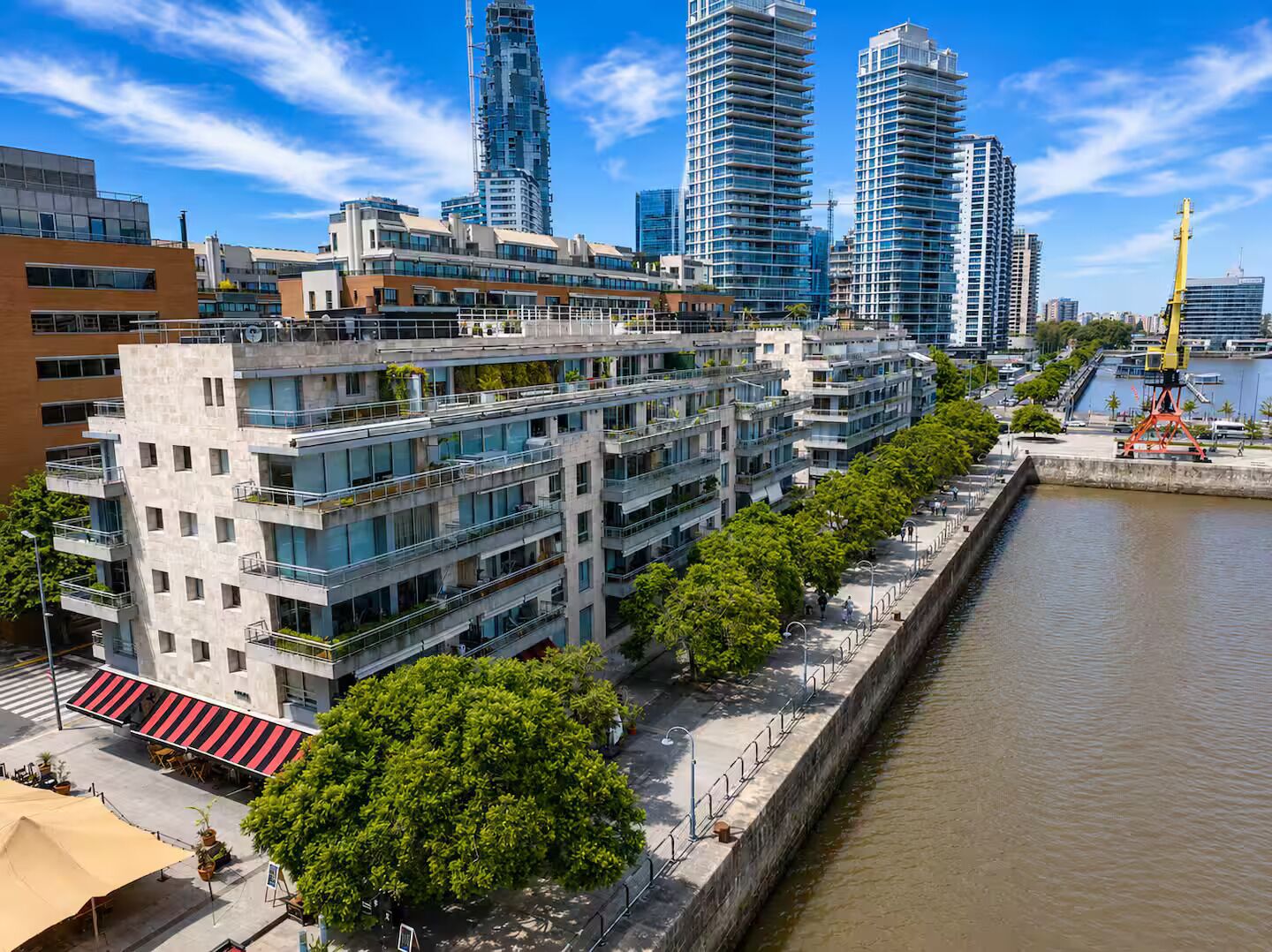 A modern urban waterfront with high-rise buildings, a pedestrian walkway, and a river.