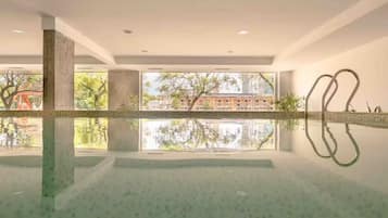 A modern indoor pool with clear reflections, large windows, and a view of a building and trees.