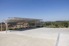 A covered outdoor area with a paved floor, surrounded by buildings and greenery. - Casa Saudade - Vila Serena (Caldas da Rainha)