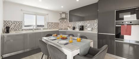A modern kitchen with grey cabinetry, a white countertop, and a dining area with grey chairs.