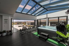 Una moderna veranda interna con tetto in vetro, vasca idromassaggio, area salotto e piante in vaso.