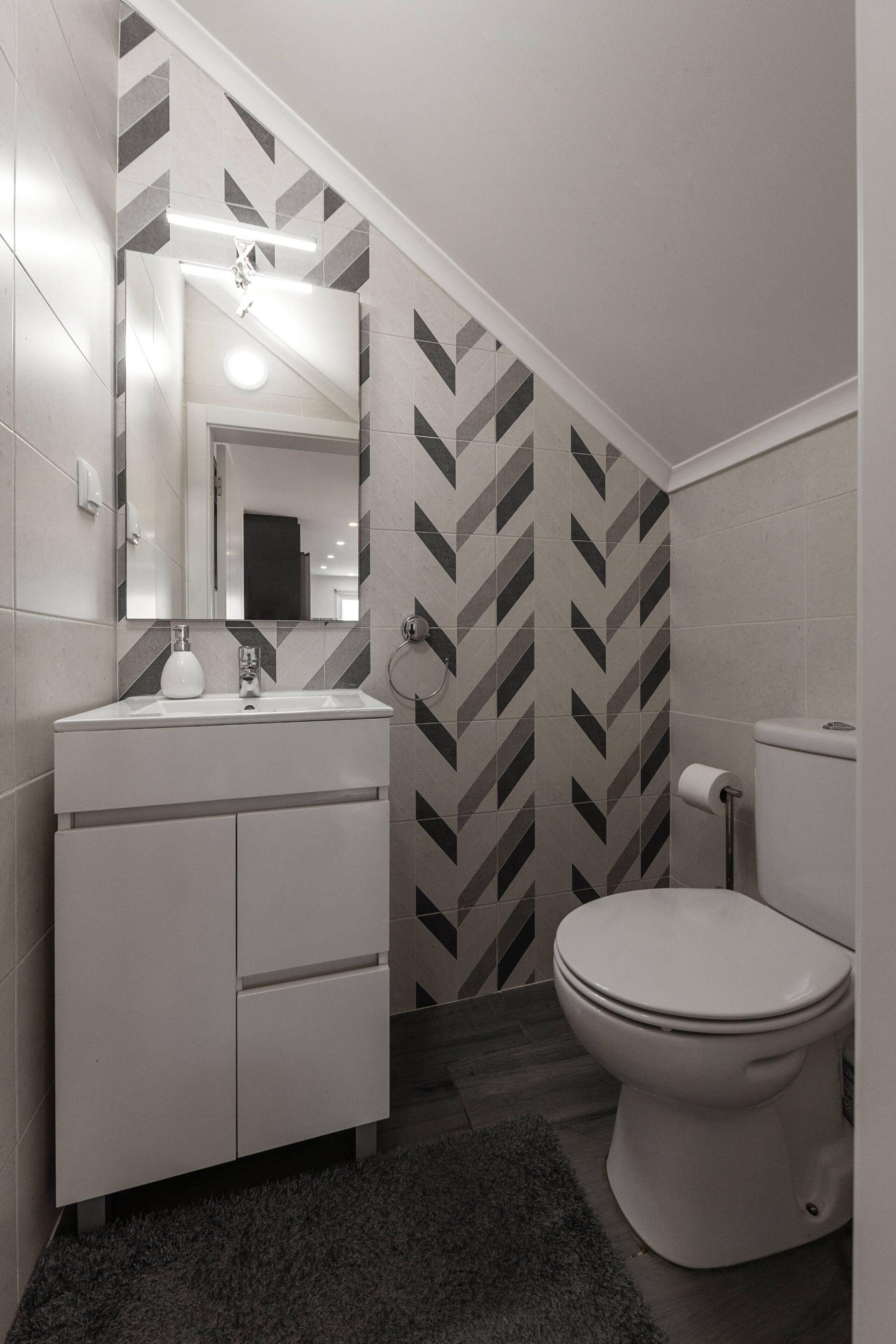 A modern bathroom with a white vanity, a mirror, a toilet, and a patterned wall.