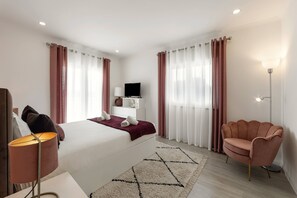 Ein Hotelzimmer mit Bett, Fernseher, Schreibtisch mit Lampe, Stuhl und Stehlampe.