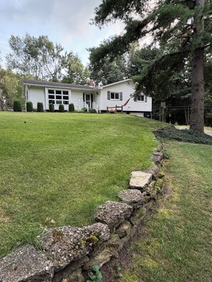 A two-story house with a stone retaining wall in front. - Forest healing, rest and relaxation await surrounded by acres of forest & lakes. (Sturgis)