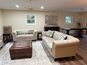 Ein Wohnzimmer mit zwei Ledersofas, einem braunen Hocker, einem Holztisch, einem großen abstrakten Gemälde und einer Kristallleuchter.