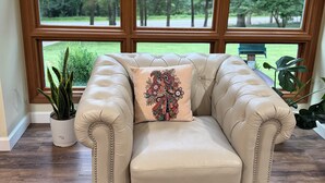 Una poltrona in pelle beige con un cuscino decorativo, posizionata di fronte a una grande finestra che si affaccia su un paesaggio verde.