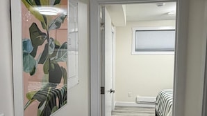 A hallway with a door leading to a bedroom with a bed and a window.