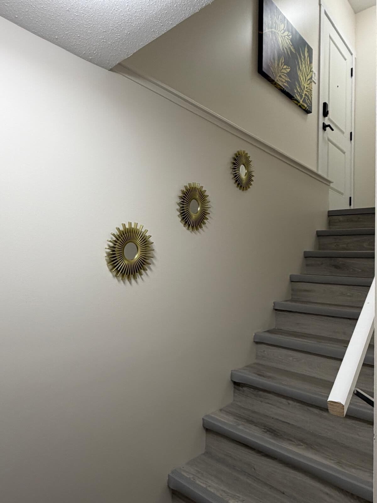 Una escalera con barandilla, una pared con tres espejos radiantes colgados y una puerta con timbre.