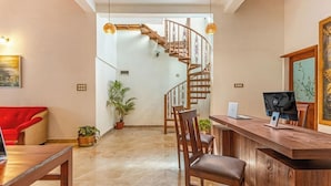 A modern interior with a wooden reception desk, a red chair, a staircase, and a potted plant. - Brook Stone Villas By Rai Hospitality (Madikeri)