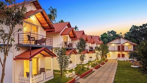 A row of bungalow-style accommodations with balconies, a paved walkway, and a well-maintained lawn. - Brook Stone Villas By Rai Hospitality (Madikeri)