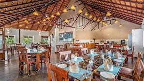 A spacious dining area with multiple tables and chairs, a high ceiling with exposed beams, and hanging pendant lights. - Brook Stone Villas By Rai Hospitality (Madikeri)