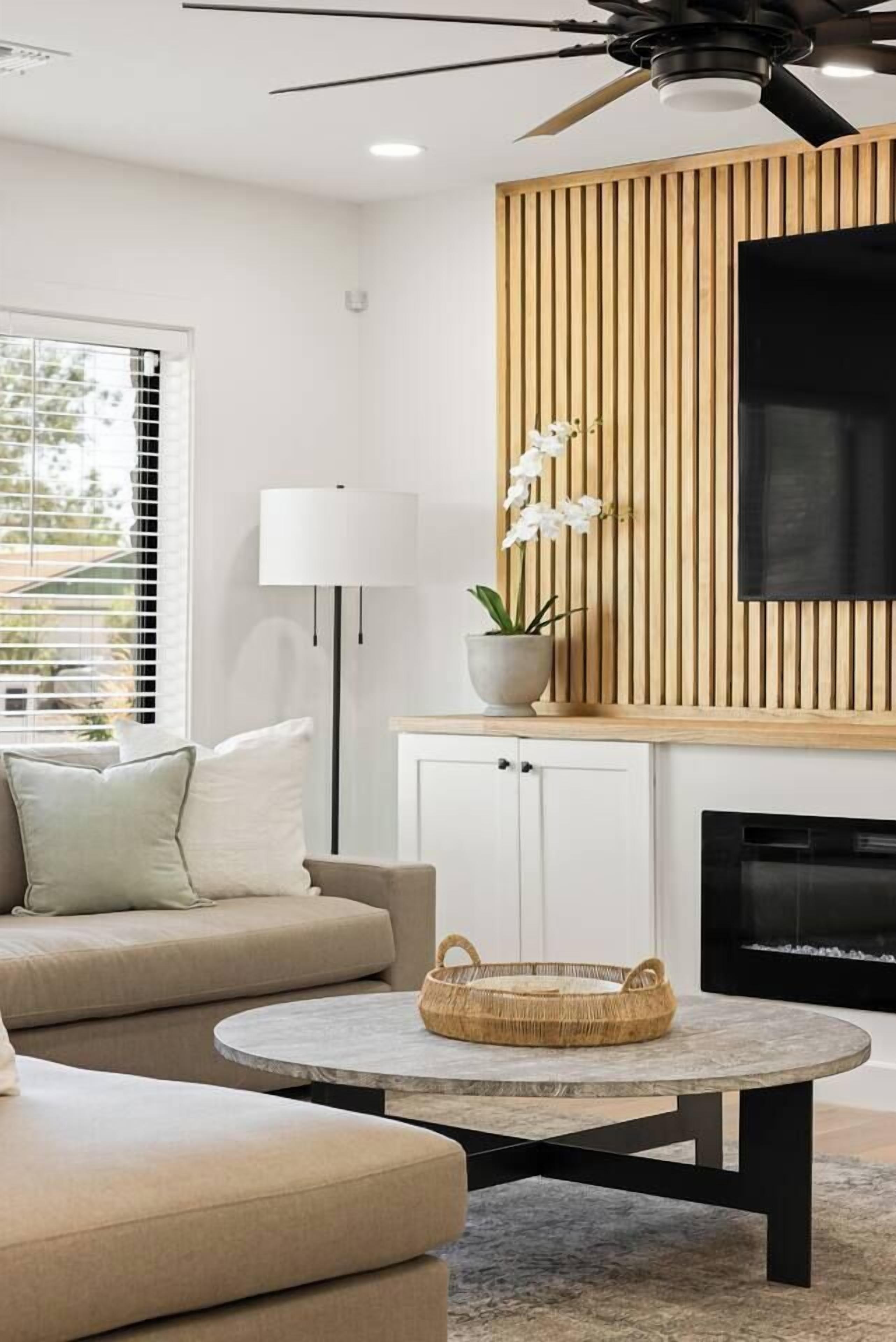 A modern living room with a sofa, a round coffee table, a TV mounted on a wooden panel wall, and a fireplace.