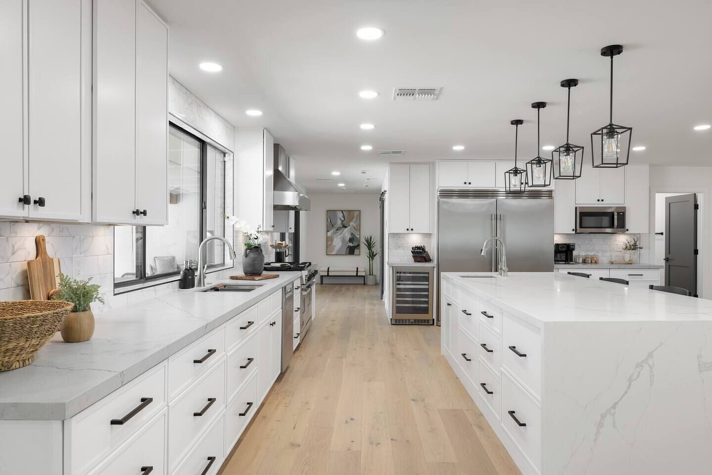 A modern kitchen with white cabinetry, a large island, stainless steel appliances, and pendant lighting.