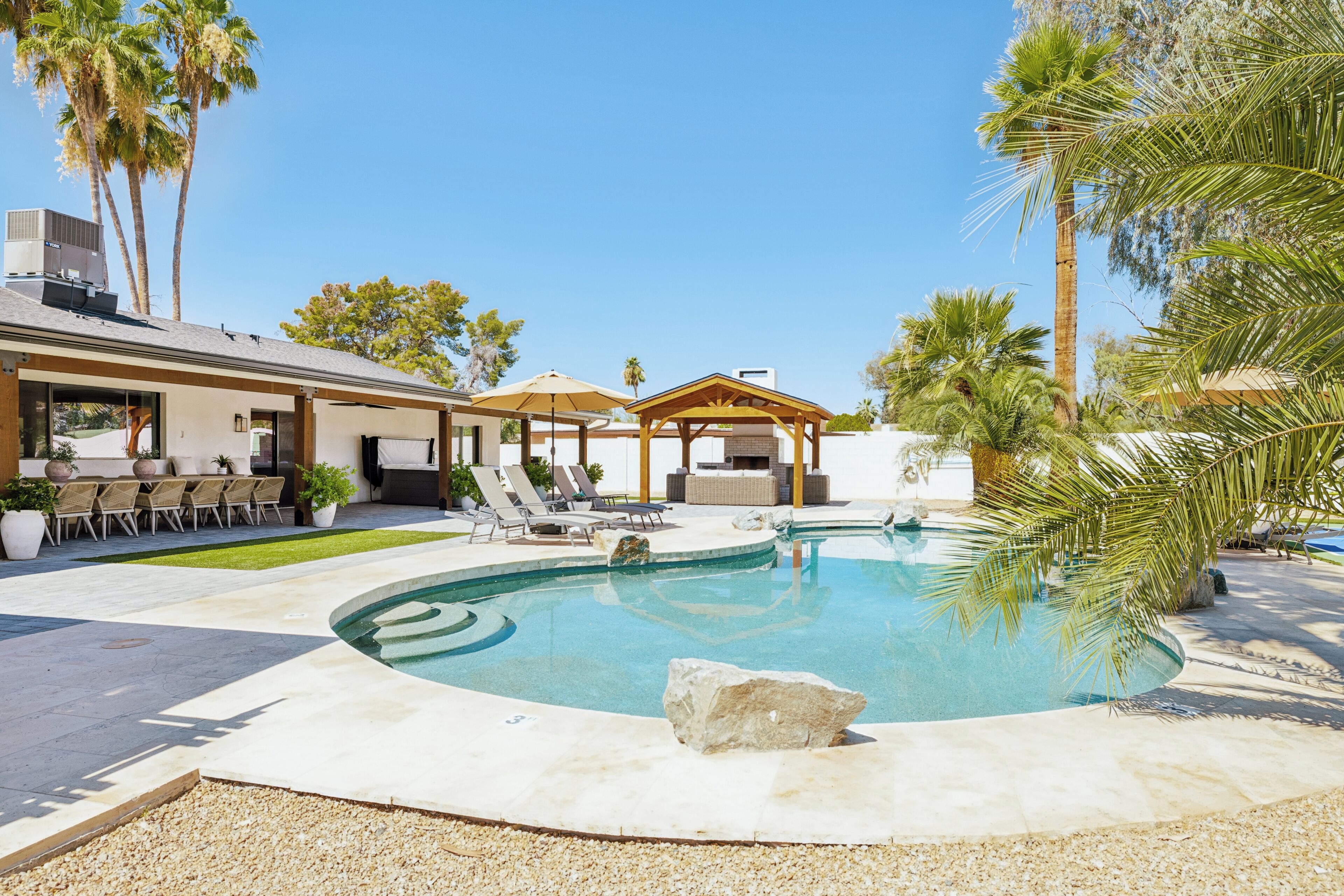 Une piscine dotée d’une terrasse en bois, de chaises longues et d’une pergola.