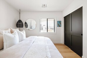 Ein Schlafzimmer mit einem Bett, einem runden Spiegel, einem Fenster mit Jalousien und einer Tür.