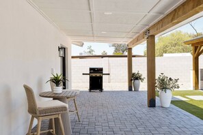 Eine Terrasse im Freien mit Grill, zwei Korbstühlen und Blumentöpfen.