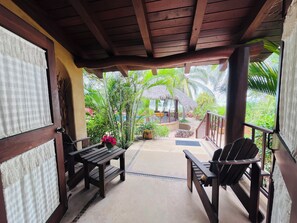 A covered outdoor seating area with wooden furniture, a thatched-roof structure, and lush greenery in the background. - Casa Sol y Luna 
Private Beachfront Suits with Pool and Ocean View (Troncones)
