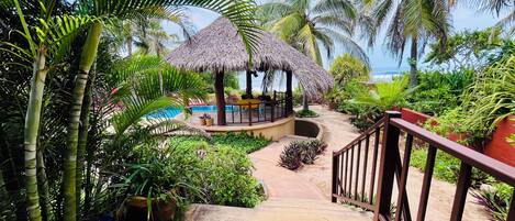 A tropical resort with a pool, thatched-roof structures, and lush greenery.
