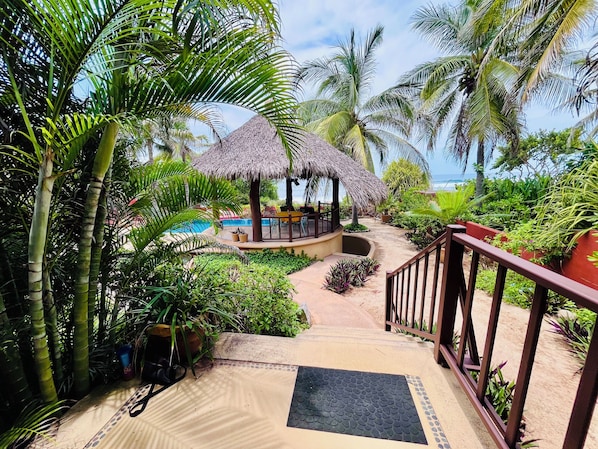 A tropical resort with a pool, thatched-roof structures, and lush greenery.