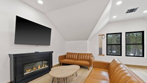 Una sala de estar moderna con chimenea, sofás de cuero, televisor montado en la pared y ventanas amplias.