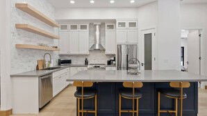 Una cocina moderna con armarios blancos, un refrigerador de acero inoxidable y una isla central con taburetes de bar.