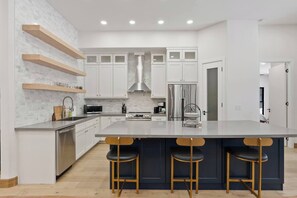 A modern kitchen with white cabinets, a stainless steel refrigerator, and a central island with bar stools. - Huckleberry Peak Villa -Glacies Montana-Game Room (Hungry Horse)