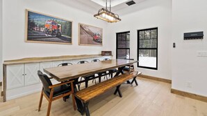 Un comedor con una mesa de madera y bancos, una lámpara colgante y dos cuadros en la pared.