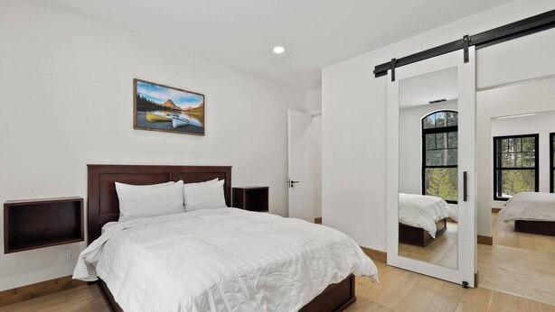 Un dormitorio con cama, mesitas de noche, un cuadro y una puerta corrediza que da a otra habitación.