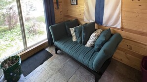 Una habitación con interior de madera, un sofá verde, un ventilador de techo, un ventanal grande y una bandera en la pared.