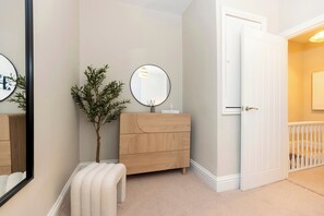 A hallway with a wooden dresser, a mirror, a potted plant, and a door leading to another room. - Gateshead 3BR Stay | Modern & Contractor Friendly (Ryton)