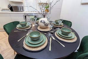 A round dining table set with green plates, bowls, and cutlery, accompanied by wine glasses and a decorative vase. - Gateshead 3BR Stay | Modern & Contractor Friendly (Ryton)