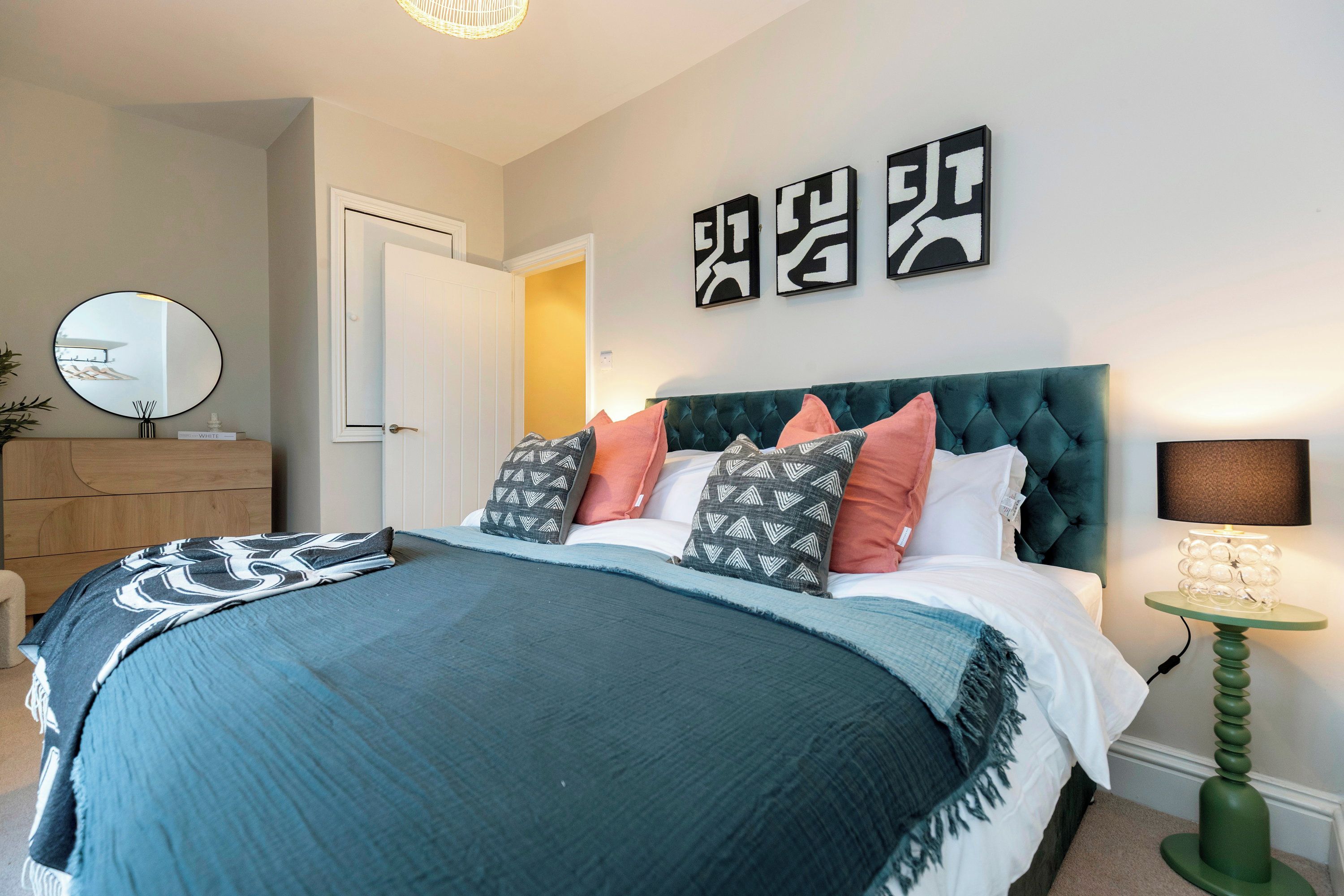 Un dormitorio con cama, cómoda, espejo y una pared con arte abstracto.
