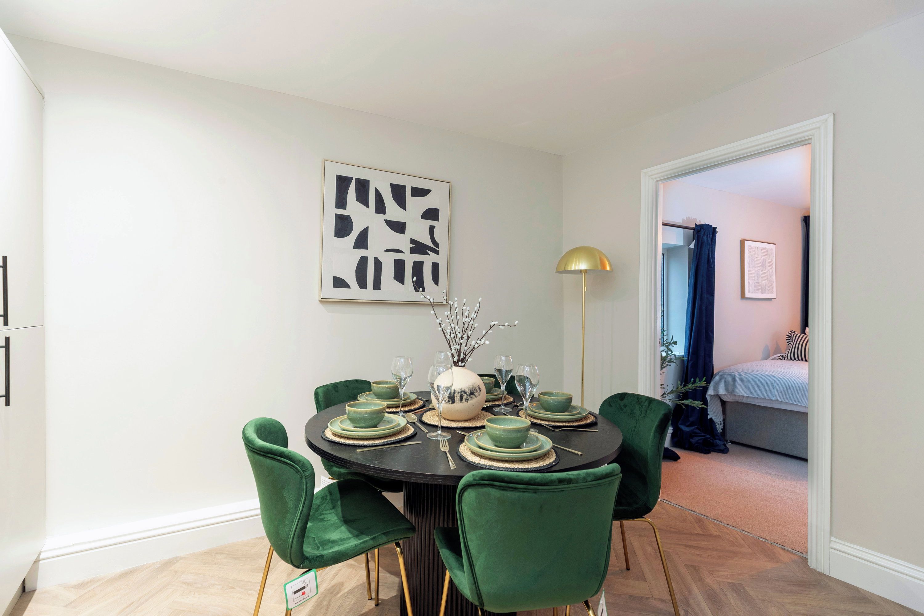 A dining area with a round table, green chairs, and a modern lamp.
